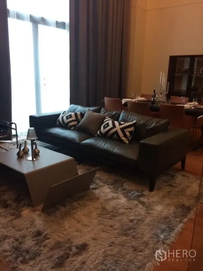 Condominium for rent in Khlong Toei, Bangkok - Contemporary living room featuring a leather sofa, plush rug, and modern coffee table beside the dining area.