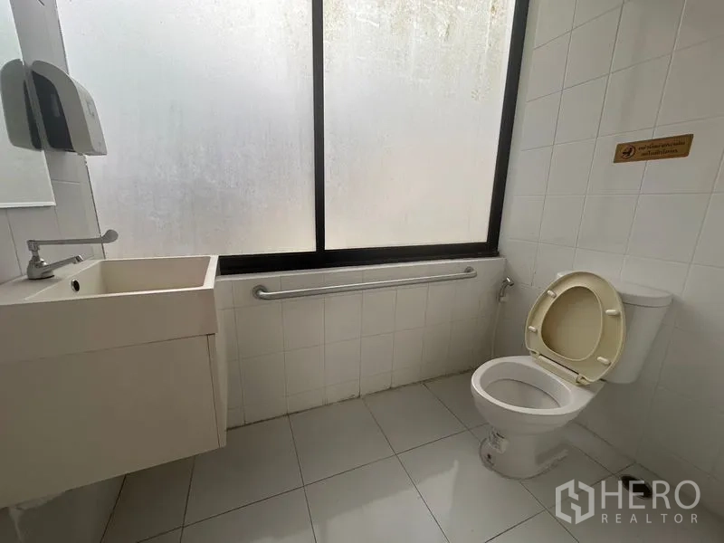 Office Space for rent in Bang Rak, Bangkok - Second restroom with frosted window, wall-mounted sink, toilet, and safety handrail.