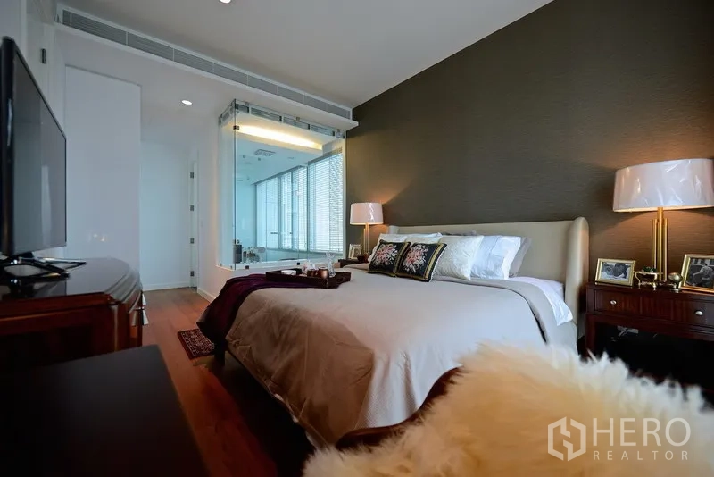 Condominium for rent in Pathum Wan, Bangkok - Spacious master bedroom with feature wall, TV unit and a glass-walled ensuite bathroom.