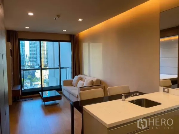 Condominium for rent in Bang Rak, Bangkok - Open-plan living room with sofa, kitchenette island and sliding balcony doors.