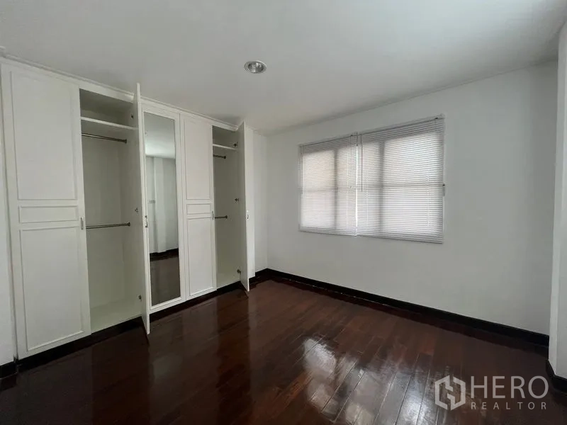 Detached House for rent in Saphan Sung, Bangkok - Empty bedroom with white built-in wardrobes, mirrored door and dark wooden floor.
