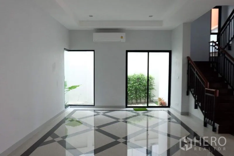 Detached House for sale in Bang Phli, Samut Prakan - Spacious living area with patterned tile floor, large windows and a wooden staircase.