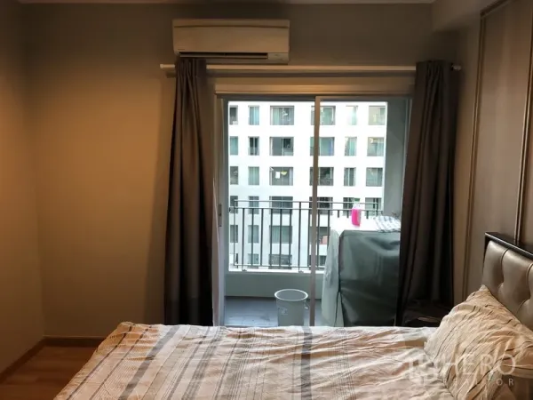 Condominium for rent in Pathum Wan, Bangkok - Bedroom with sliding doors to a small balcony and air conditioning, facing neighboring building.
