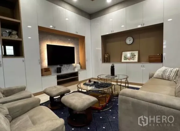 Townhouse for rent in Yan Nawa, Bangkok - Living room with glossy white built-in cabinets, wall-mounted TV, and nested coffee tables.