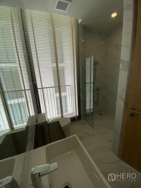 Condominium for rent in Watthana, Bangkok - Modern bathroom with vanity, glass shower and window blinds.