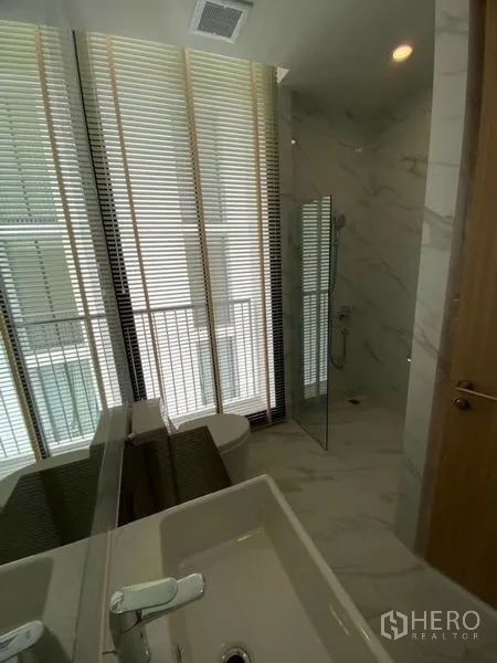 Condominium for rent in Watthana, Bangkok - Modern bathroom with vanity, glass shower and window blinds.