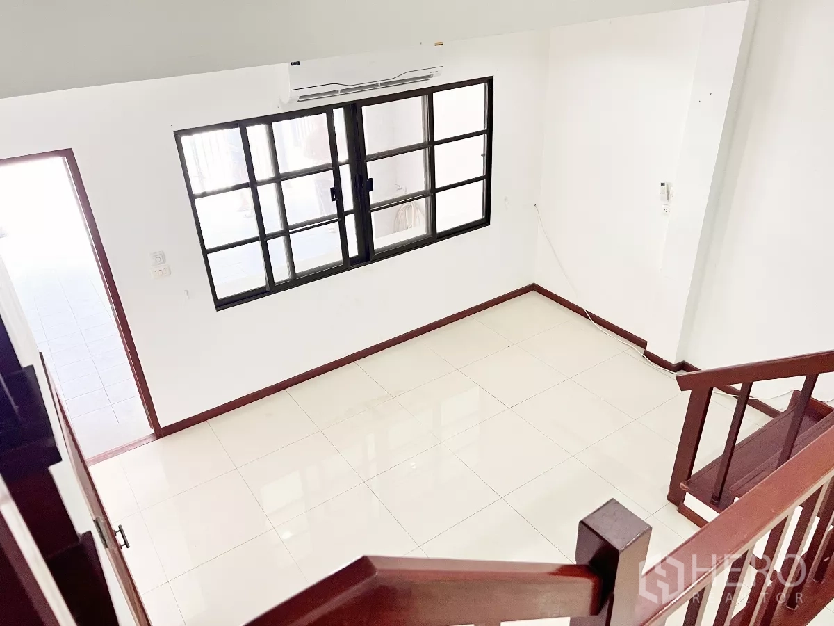 Townhouse for rent or sale in Phra Khanong, Bangkok - View from staircase to bright landing with tiled floors and sliding windows.