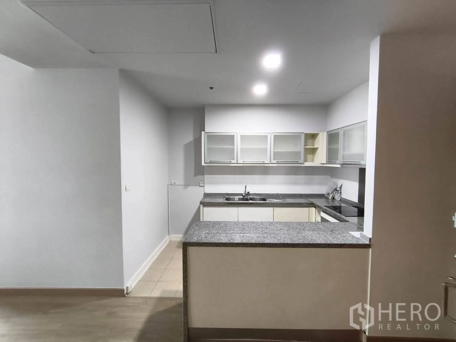 Condominium for rent in Khlong Toei, Bangkok - U-shaped kitchen with granite countertops, sink, cooktop, and glass-front wall cabinets.