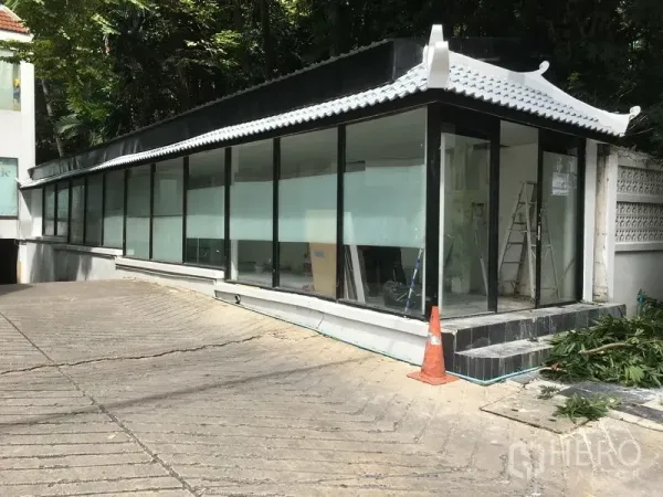 พื้นที่ขายปลีก ให้เช่าในWatthana, Bangkok - หน้าร้านกระจกมุมอาคาร ชายคาดำขาว บันไดทางเข้าเล็ก และทางลาด ท่ามกลางต้นไม้ร่มรื่น