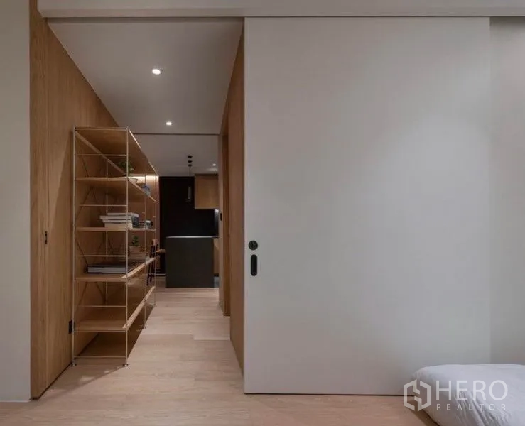 Condominium for rent in Phaya Thai, Bangkok - Hallway with large sliding door, minimalist shelving and wood flooring leading to the kitchen.