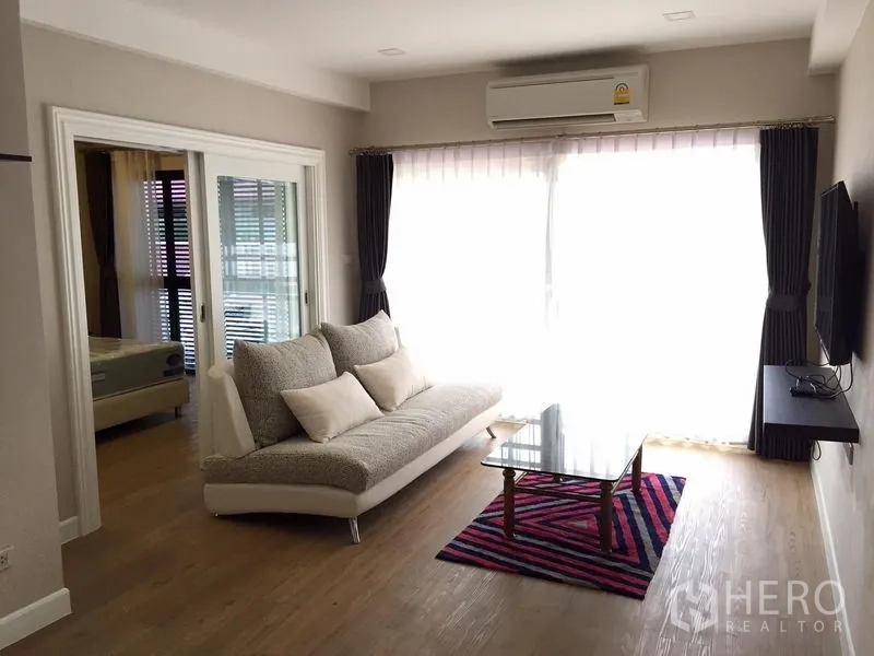 联排别墅 出租在Khlong Toei, Bangkok - 明亮客厅，沙发、电视墙、空调与落地窗帘。