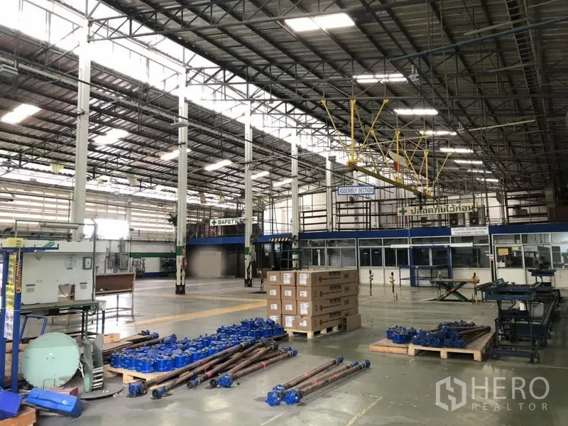 工厂 出租在Lam Luk Ka, Pathum Thani - 装配区摆放托盘与设备，旁有玻璃隔间办公室与高净空行车系统。