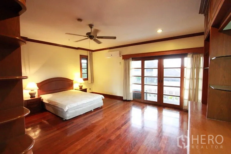 独立式住宅 出租在Prawet, Bangkok - 大卧室配吊扇、木地板与法式玻璃门，通往阳台。