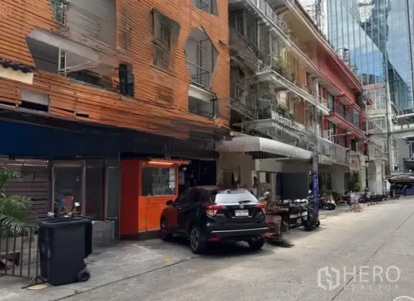 Retail Space for rent in Watthana, Bangkok - Quiet side street lined with shophouses and a nearby high-rise office tower, showing convenient access and parking.