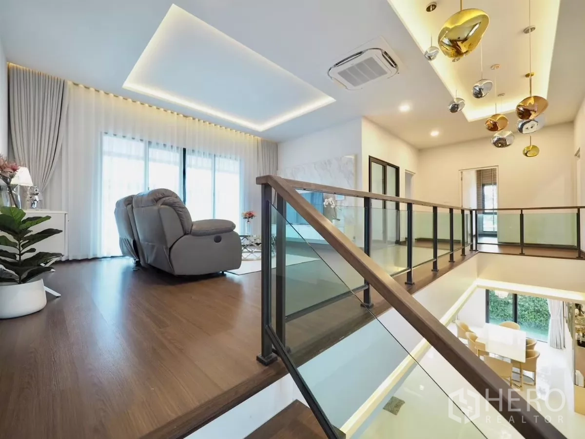 独立式住宅 出租在Bang Phli, Samut Prakan - 楼梯旁家庭起居区，木地板与玻璃扶手。