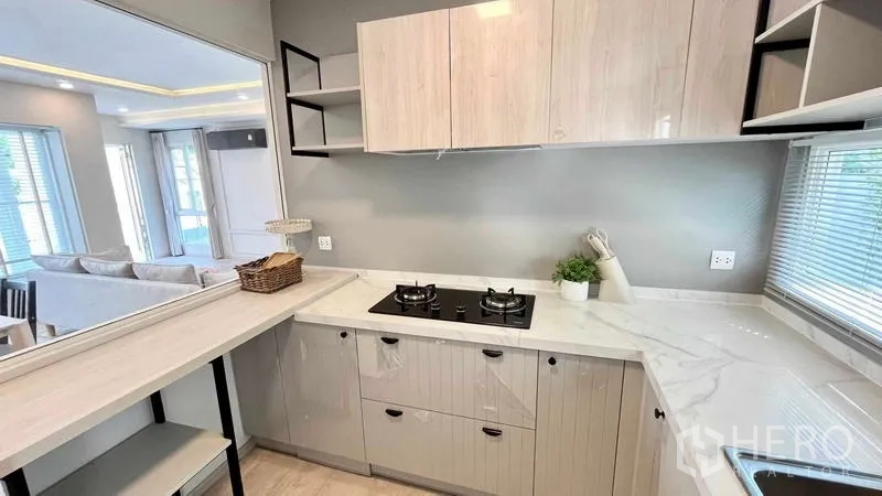 Detached House for rent or sale in Prawet, Bangkok - L-shaped kitchen with gas hob, marble-look countertops and upper cabinets.