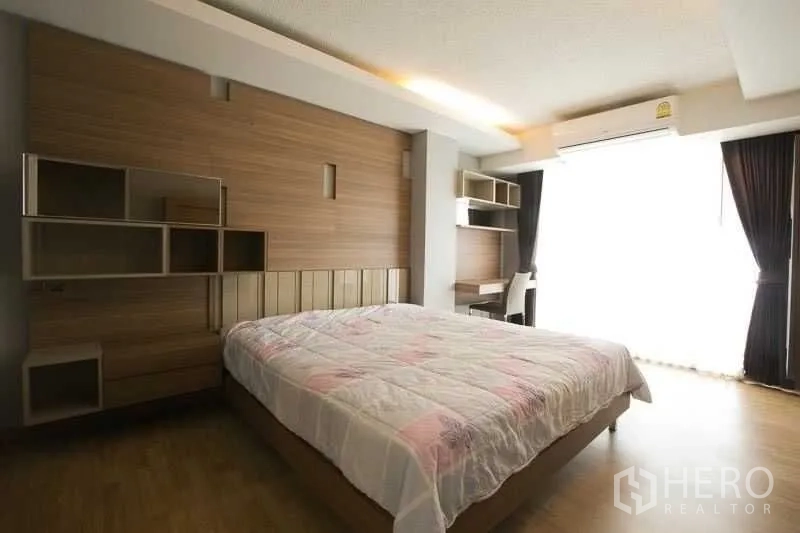 Condominium for rent in Khlong Toei, Bangkok - Spacious master bedroom featuring wood accent wall, study desk and wide window.