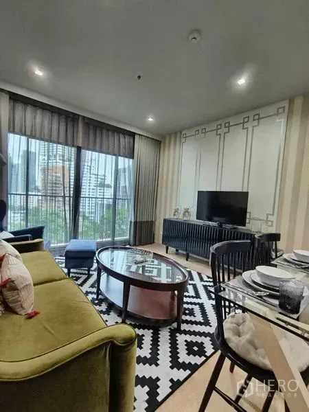 公寓 出租在Bangkok - 开放式客餐厅，绿色沙发与玻璃茶几，阳台可眺望素坤逸天际线。