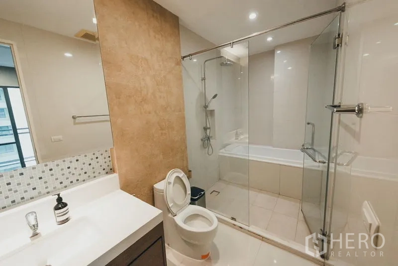 Condominium for rent in Khlong Toei, Bangkok - Main bathroom with glass partition, shower and bathtub combination, vanity and toilet.