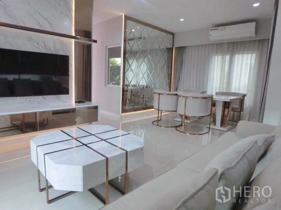 Detached House for rent in Bang Khen, Bangkok - Open-plan living and dining with marble TV wall, geometric coffee table and mirrored partition.