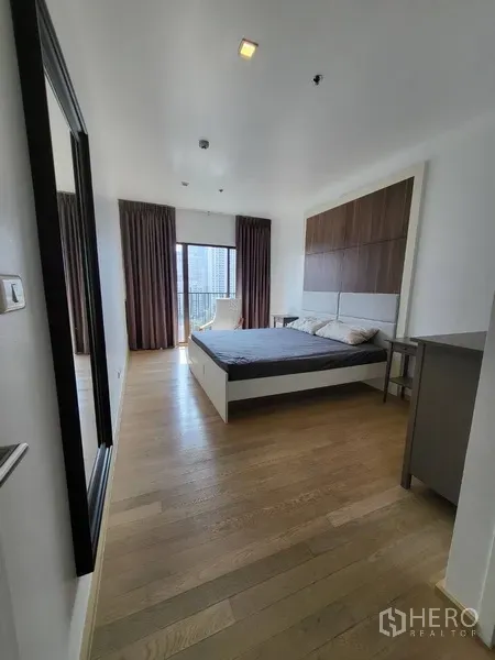 Condominium for rent in Bangkok - Spacious bedroom with wood floors and a large window leading to a city-view balcony.