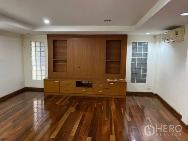 Townhouse for sale in Phra Khanong, Bangkok - Spacious living room with built-in media wall, glass-block side windows, and hardwood floors.