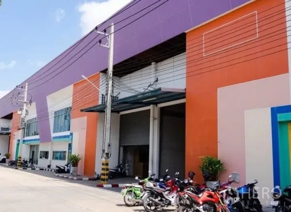 โรงงาน ให้เช่าในMueang Samut Sakhon, Samut Sakhon - ด้านหน้าโรงงานสีสันสด พร้อมประตูม้วนขนาดใหญ่ หลังคากันสาดและพื้นที่จอดรถในสมุทรสาคร