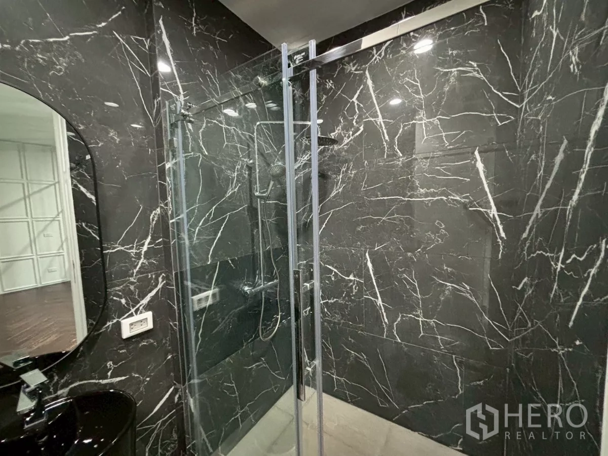 Condominium for sale in Bang Kho Laem, Bangkok - Modern bathroom clad in black marble with a glass shower enclosure and oval mirror.