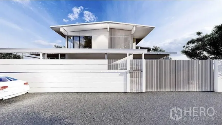 Detached House for rent in Lat Phrao, Bangkok - Modern two-storey detached house with white facade and tall privacy fence along a paved driveway under blue sky in Lat Phrao.