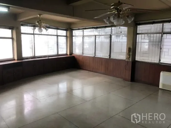 Shophouse for rent in Khlong Toei, Bangkok - Spacious upper-floor room with wraparound windows, ceiling fans and a built-in wood ledge.