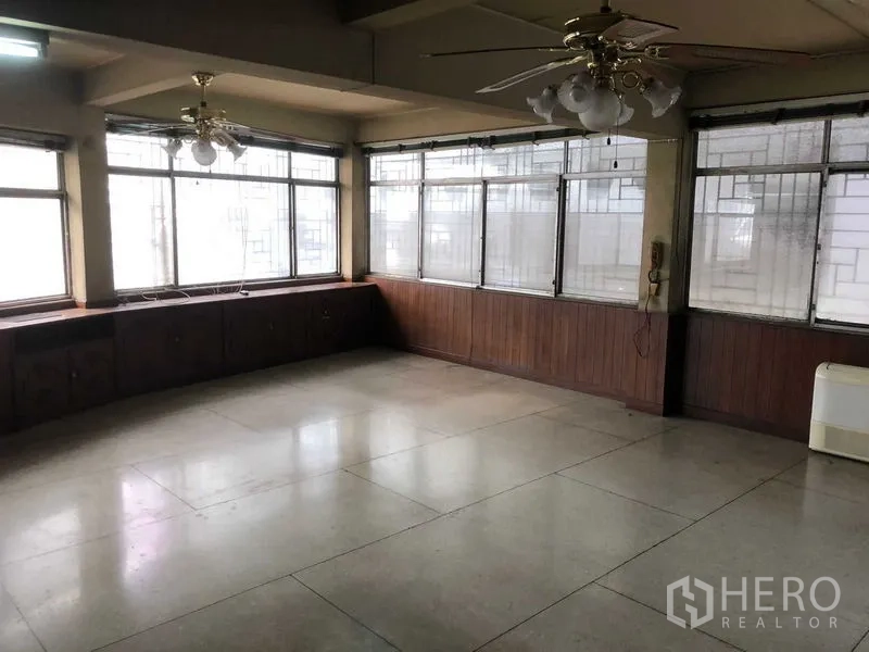 Shophouse for rent in Khlong Toei, Bangkok - Spacious upper-floor room with wraparound windows, ceiling fans and a built-in wood ledge.