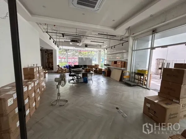 办公空间 出租在Khlong Toei, Bangkok - 一层开放式办公区，通高落地窗、人字形地板、轨道灯，现场堆放纸箱。