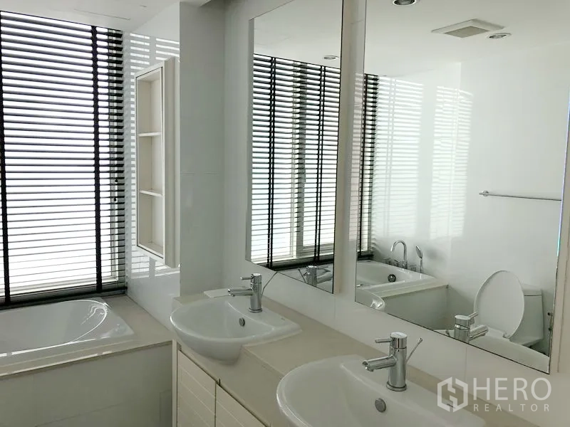 Condominium for rent in Khlong Toei, Bangkok - Modern bathroom with double vanity, large mirrors, bathtub, and window blinds.