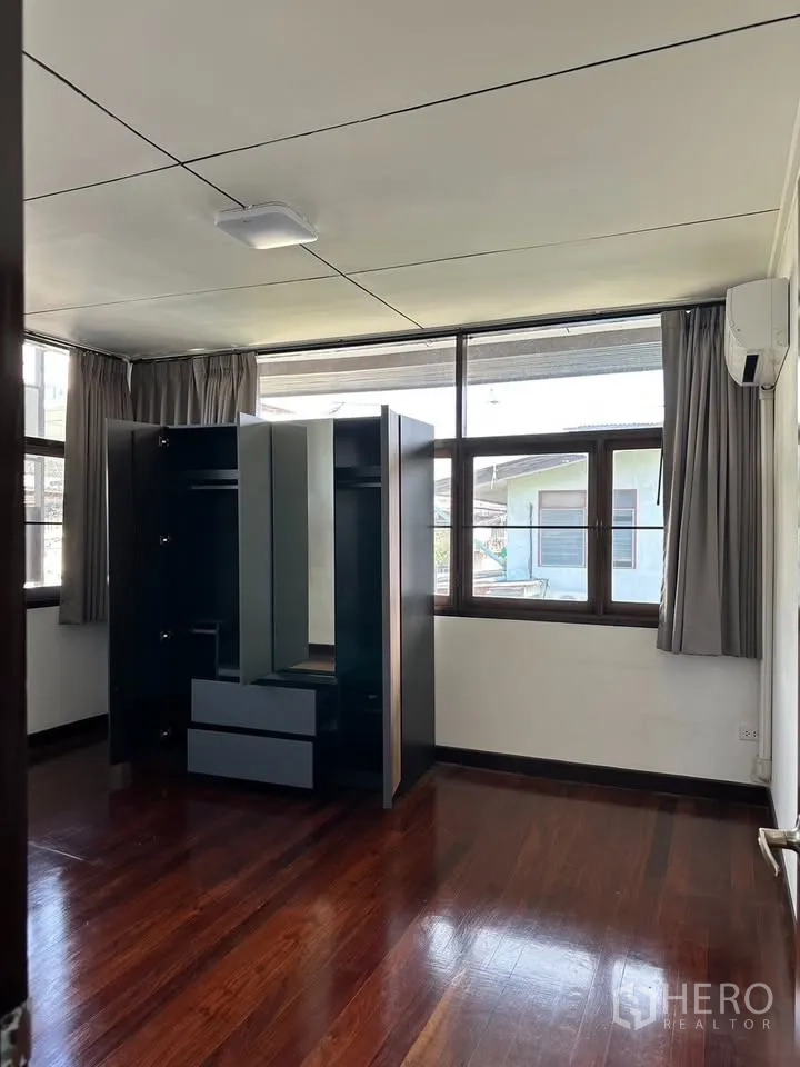 Detached House for rent in Phra Khanong, Bangkok - Upstairs bedroom with polished wood flooring, large windows and freestanding wardrobe.