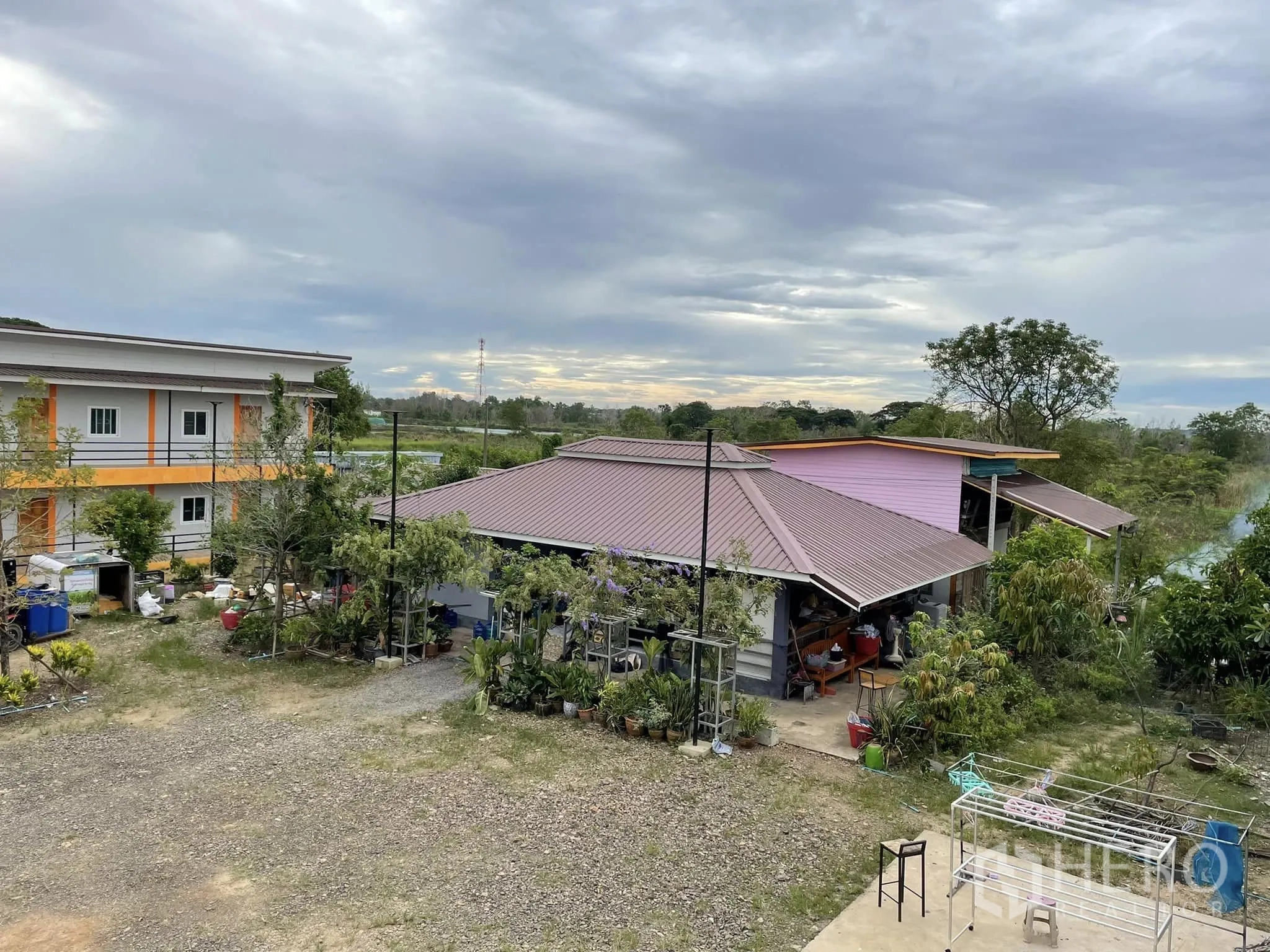 Warehouse for rent or sale in Pathum Thani - Garden area with pitched-roof house beside the apartment block and open yard.