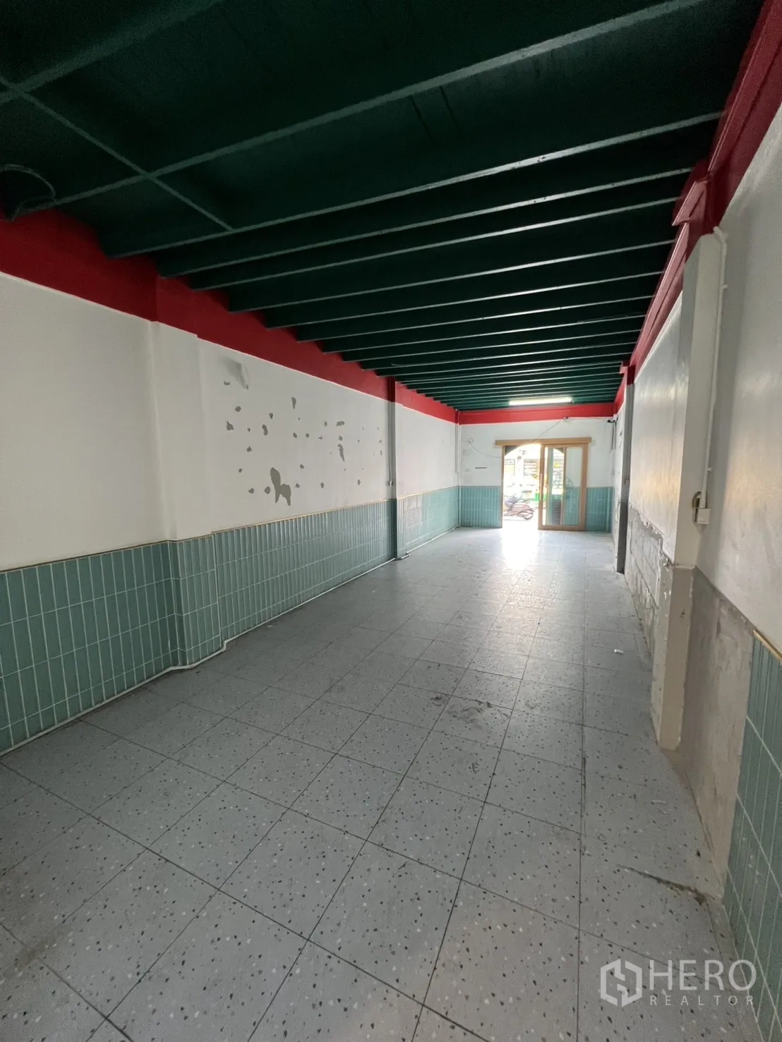 Shophouse for rent in Watthana, Bangkok - Long ground-floor retail space with teal ceiling beams, white walls and tiled floor.