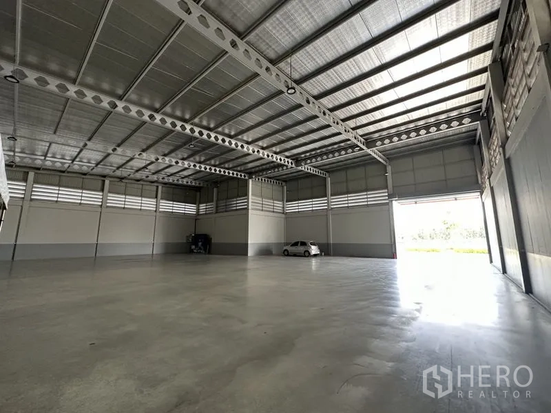 Factory for rent or sale in Lam Luk Ka, Pathum Thani - Open-plan production hall facing a large roller door allowing natural light.