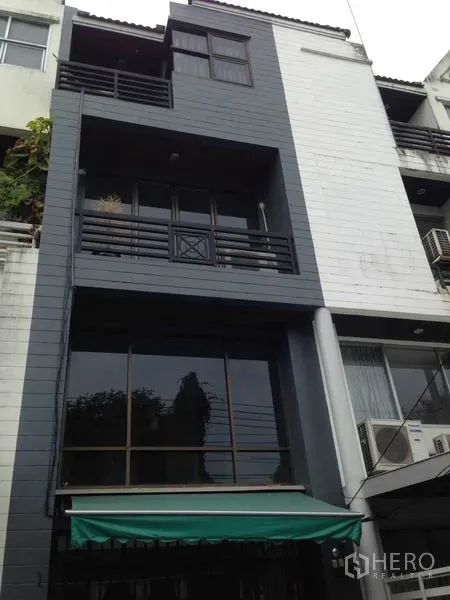 带办公室的家 出租或出售在Wang Thonglang, Bangkok - 旺通朗四层居家办公楼立面，带阳台、大窗与绿色遮阳篷。