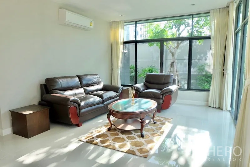 独立式住宅 出租在Prawet, Bangkok - 明亮客厅，皮沙发、茶几与面向花园的落地窗