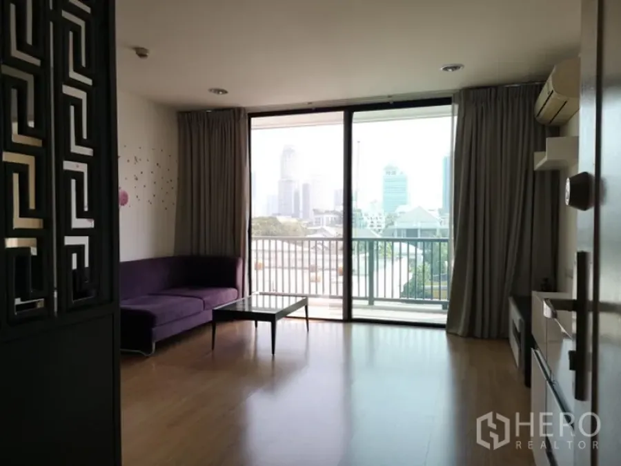 公寓 出售在Watthana, Bangkok - 明亮客厅，落地窗与阳台，紫色沙发与木地板，远眺城市天际线