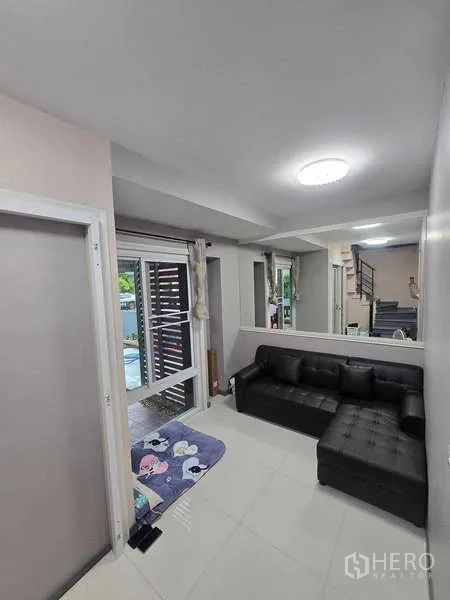 独立式住宅 出租在Lat Krabang, Bangkok - 小客厅，黑色皮沙发、落地窗，并可通往楼梯。