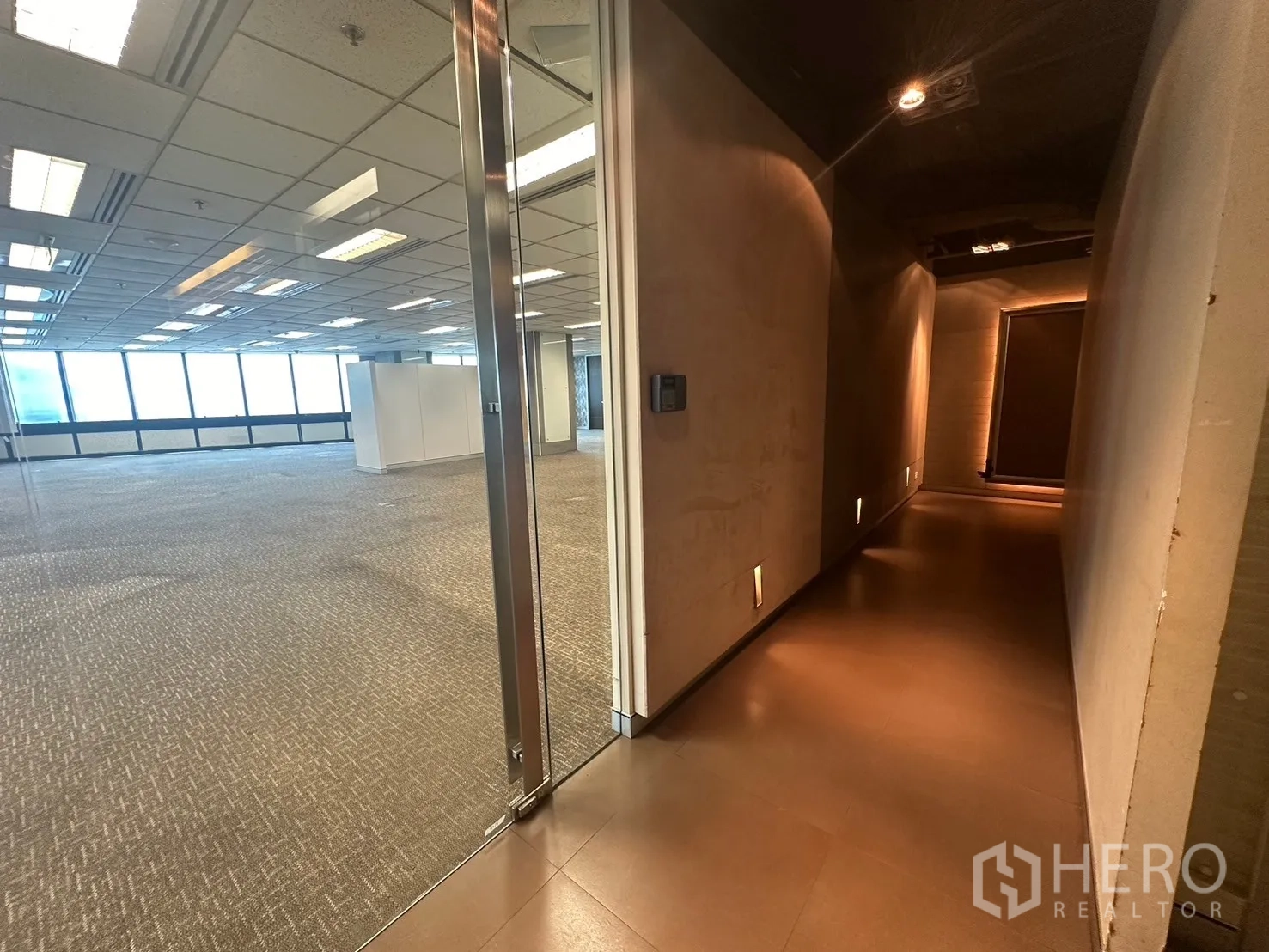 Office Space for rent in Khlong Toei, Bangkok - Glass entry from a warm-lit corridor to a large open-plan workspace with windows.