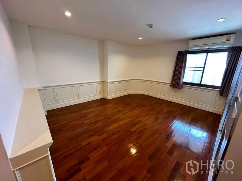 Condominium for rent in Bangkok - Cozy bedroom with wainscoting detail, window and wall-mounted air conditioner.