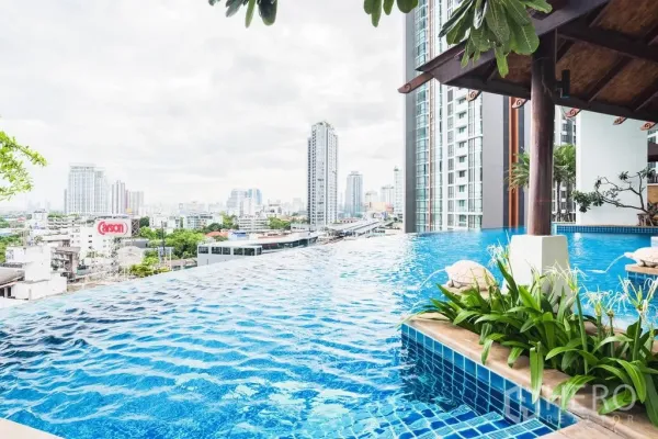 Condominium for rent in Watthana, Bangkok - Infinity-edge swimming pool with lush plants and Bangkok city skyline backdrop.
