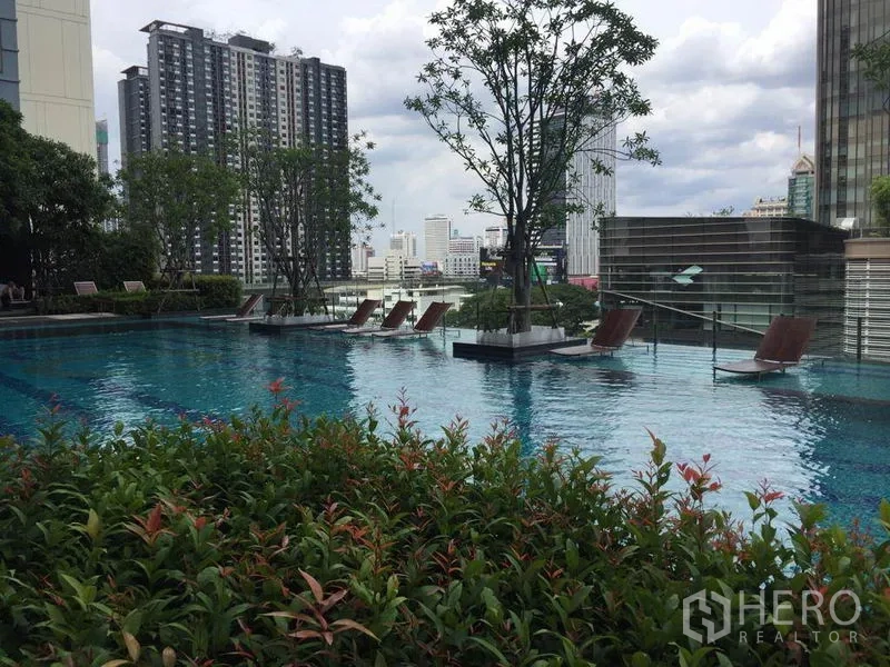 公寓 出租在Ratchathewi, Bangkok - 屋顶泳池配躺椅与绿植，背景是城市天际线。