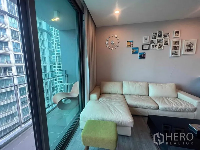 Condominium for rent in Khlong Toei, Bangkok - L-shaped sofa beside a glass-railed balcony with views of a neighboring tower.