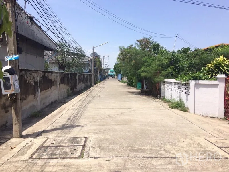 Warehouse for rent in Samut Prakan - Quiet concrete access road with utility poles leading to a warehouse area.