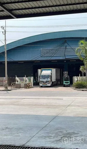 Warehouse for rent in Si Racha, Chon Buri - Covered loading bay of a blue-roof warehouse with a truck and forklifts at the dock.