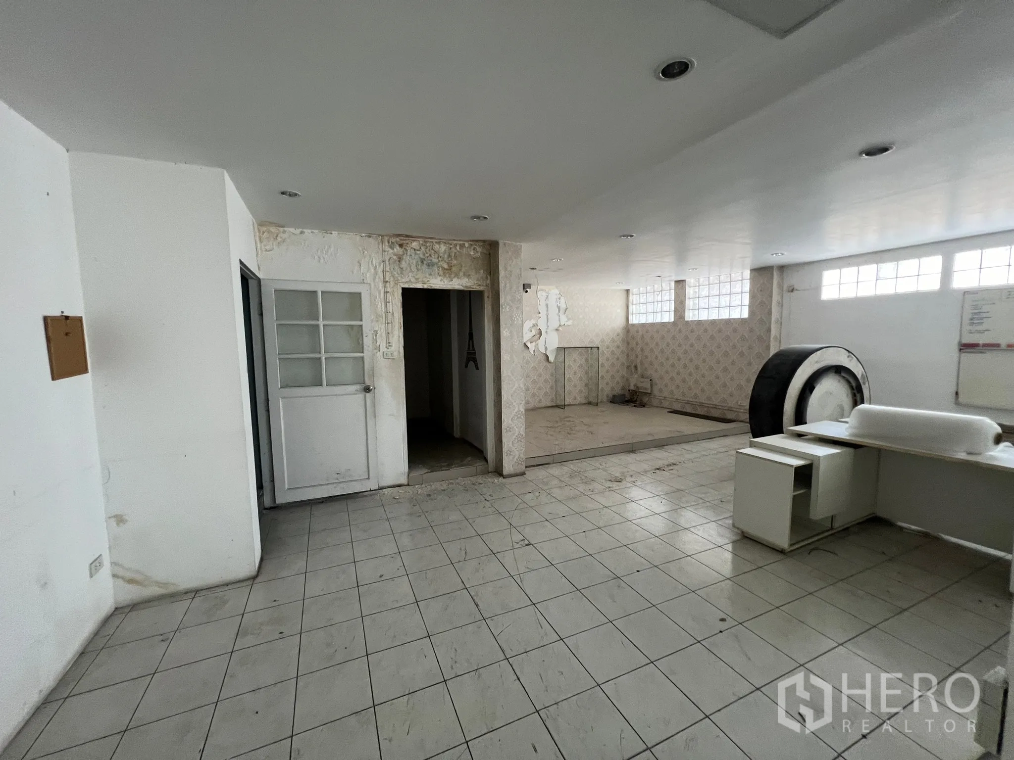 Shophouse for rent in Khlong Toei, Bangkok - Large work area with tiled flooring, storage rooms and worn plaster walls.