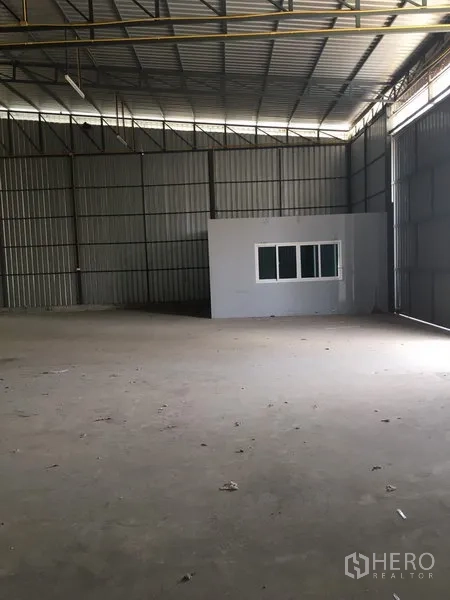 Warehouse for rent in Bang Kapi, Bangkok - Warehouse bay showing a built-in office with window, tall corrugated metal walls, and wide sliding access door.